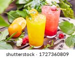 Glasses with fresh lemonade in summer greenery and flowers on the background of a wooden table, citrus and berry lemonade with frappe ice on a wooden table top on the background of a summer garden