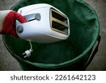 Throw old household appliances in the trash.A hand throws a sandwich toaster into a bucket.Disposal of kitchen appliances.