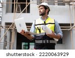 Small photo of CAucasian Man Worker in a construction site. Architecture engineering holding a laptop on building site checking plans. Successful engineer or architect, Joyous businessman. Construction worker.