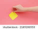 Woman's hand glues yellow sticker or sticky post-it notes on pink background.