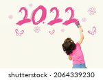 Small photo of Cute little girl writing new year 2022 with pink painting brush on wall background