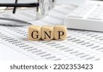 Small photo of wooden cubes with the word GNP on financial background with chart, calculator, pen and glasses, business concept.
