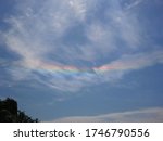 An inverted rainbow with very saturated colors, suspended among fluffy clouds under deep blue sky