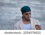 Small photo of Latin and Hispanic boy, young and nonconformist, rebellious, with a handkerchief on his head, exhaling the smoke of a cigarette rolled by himself. Concept tobacco, smoke, fire, addiction, gangs.