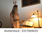 Small photo of Young, beautiful, blonde woman in flower dress, leafing through guestbook at the reception of a luxurious hotel. Concept travel, hotels, books, copy space.