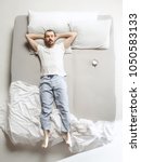 Small photo of Top view photo of young man sleeping in a big white bed. Emotions concept. Morning after sleep. Happy man on the bed. alarm clock and unwillingness to wake up