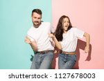 A couple of young funny and happy man and woman dancing hip-hop at studio on blue and pink trendy color background. Human emotions, youth, love and lifestyle concept