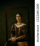 Small photo of Portrait of a antic girl wearing a princess or countess dress over dark studio. portrait through picture frame