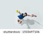 Young woman in blue shirt playing tennis. She hits the ball with a racket. Indoor studio shot isolated on white. Youth, flexibility, power and energy. Negative space. Top view.