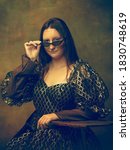 Small photo of Eyewear black. Young woman as Mona Lisa, La Gioconda isolated on dark green background. Retro style, comparison of eras concept. Beautiful female model like classic historical character, old-fashioned