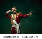 Small photo of Shoting duelist. Young man in suit as Nicholas II isolated on dark green background. Retro style, comparison of eras concept. Beautiful male model like historical character, monarch, old-fashioned.
