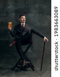 Small photo of Fashion king. Young man with glass of beer in art action remaking greatest artist Salvador Dali and its pictures isolated on vintage background. Retro style, comparison of eras, fashionable characters