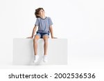 Looking up. Little Caucasian preschool boy sitting on box isolated over white studio background. Copyspace for ad. Happy childhood, education, emotions, facial expression concept. Having fun