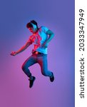 Small photo of Jumping, flying. Stylish young asian man isolated over lilac color studio background in pink neon light. Concept of human emotions, facial expression, youth culture, diversity. Listening to music