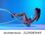 Small photo of Young sportive girl training with sports equipment isolated on gradient blue-pink studio background in neon light. Modern sport, action, motion, youth concept. Fitness, hobby, healthy lifestyle