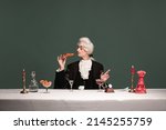 Small photo of French breakfast. Portrait of young elegant man in peruke and vintage jacket sitting at table isolated on dark green background. Retro style, comparison of eras concept.