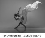 Small photo of Art and beauty of male body. Black and white portrait of graceful muscled male ballet dancer dancing with fabric, cloth isolated on grey studio background. Grace, health, strength