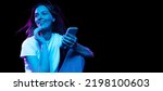 Small photo of Online shopping. Happy young pretty girl with cellphone isolated on dark background in purple neon light. Concept of emotions, facial expression, youth, aspiration.