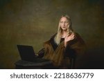 Small photo of Remote work. Shocked young charming girl in image of Mona Lisa, La Gioconda using laptop isolated on dark green background. Creative art, beauty, style, imitation, eras comparison