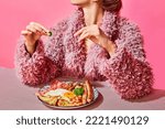 Small photo of Woman in furry pink coat eating English breakfast with eggs, bacon, sausage and vegetables. Vintage, retro style interior. Food pop art photography. Complementary colors. Copy space for ad, text
