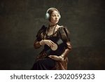 Portrait of pretty young girl, royal person in elegant vintage dress listening to music in headphones, holding vinyl on dark green background. Concept of history, renaissance art, comparison of eras