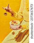 Small photo of Woman in nice outfit holding golden spoon and bowl with muesli, cereal with berries against yellow background. Concept of healthy food, nutrition, pop art style, taste. Poster. Copy space for ad