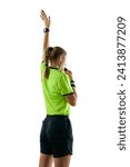 Small photo of Back view. Young serious woman, soccer referee blowing a whistle and raising hand up as free kick symbol against white studio background. Concept of sport, competition, match, profession, football