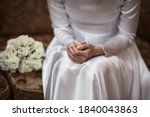 
A girl in a white satin wedding dress sits on a luxurious sofa holding a wedding bouquet. She is waiting for the groom.