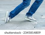 Small photo of close-up of a woman's feet in jeans and sneakers tripping over unevenly laid paving slabs. Accident, injury on a walk due to poor road surface.