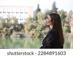 Beautiful young woman leaning over the railing of the river in Seville, Spain. The photo is taken from behind and she is looking at the horizon where you can see the other bank.