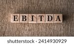 Small photo of EBITDA text written on wooden block on brown background. Short for earning before interest taxes depreciation and amortization
