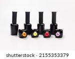 Small photo of black bottles of varnishes stand in a row along with open bottles of multicolored varnish. bright varnishes of orange, yellow, pink and lilac colors lie open on a white background