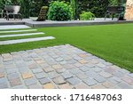 Modern garden design and terrace construction with a material mix of cobble paving stones and concrete paving slab and artificial lawn and wood