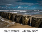 Small photo of Tytul: The photo shows a breakwater in the Baltic Sea during stormy weather. The water crashes against the breakwater structure, creating white foams and whirlpools. The clouds in the sky are heavy, a