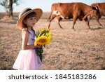 Portrait of a little pretty girl with flowers. 
Beautiful girl with sunflowers near a cow pasture.
Alpine style.