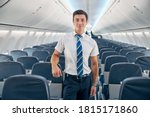 Close up portrait of handsome confident steward posing at the photo camera near the cozy chair of passenger aircraft