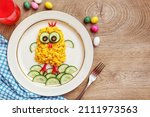 Scrambled egg easter chick made it from scrambled eggs,cucumbers,black olives and red hot peppers on plate with wooden background.Art food idea for kids Easter's breakfast.Top view.Copy space