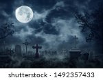 Zombie Rising Out Of A Graveyard cemetery In Spooky dark Night full moon. Holiday event halloween background concept.