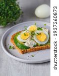 Small photo of Sandwich with avocado, egg, mayonnaise and water cress on a plate. Bright wooden background, egg in back and water cress.