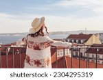 Woman in a straw hat looking over the rooftops of the Lisbon town 