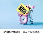 Mini shopping cart with a thirty percent discount sign and pink alarm clock on blue background. Conceptual image of sale, seasonal discounts in shopping stores, discount time	