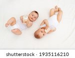 Small photo of two babies suck milk from a bottle lying in a crib in the children's room on a white bed