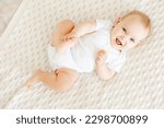 close-up of a laughing happy baby on a white cotton bed in a bright bedroom, a small smiling baby boy or girl lying on her back