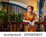 
Woman in 19th century dress and white gloves leaning on wooden handrails in hotel