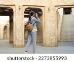 A young woman traveler with a backpack on her back walks and photographs the old narrow streets of Dubai Deira and Creek. Travel and sightseeing concept