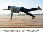 Small photo of A guy in city clothes is engaged in fitness, inept exercise, lazy gymnastics, a hipster trains at dawn, a training ground. High quality photo