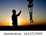 Silhouette of crane rigger working with the hook block in oilfield at sunset