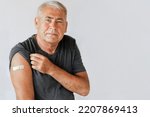 Small photo of Male Senior Smiling after Receiving Vaccine. Old Man Showing Arm with Bandage, Patch after Vaccine from COVID-19 or Monkeypox. Covid, Monkey Pox Vaccination for Older People. Gray Studio Background.