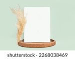 Small photo of Blank Greeting Card Invitation Mockup. Front view. Dry Pampas Grass Modern Wooden Plate, Paper Mock Up on Green Table. Copy Space. Minimal Business Brand Template. Soft Shadow. Nordic Flier Design. A6