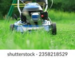 Small photo of Lawn mower cutting grass. Small grass cuttings fly out of lawnmower. Grass clippings get spewed out of a mower pushed around by landscaper. CloseUp. Gardener working with mower machine. Mowing lawns